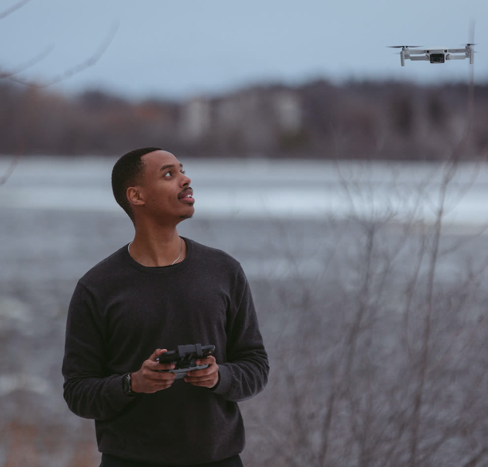 Drone operator holding a controller and watching a drone by the water